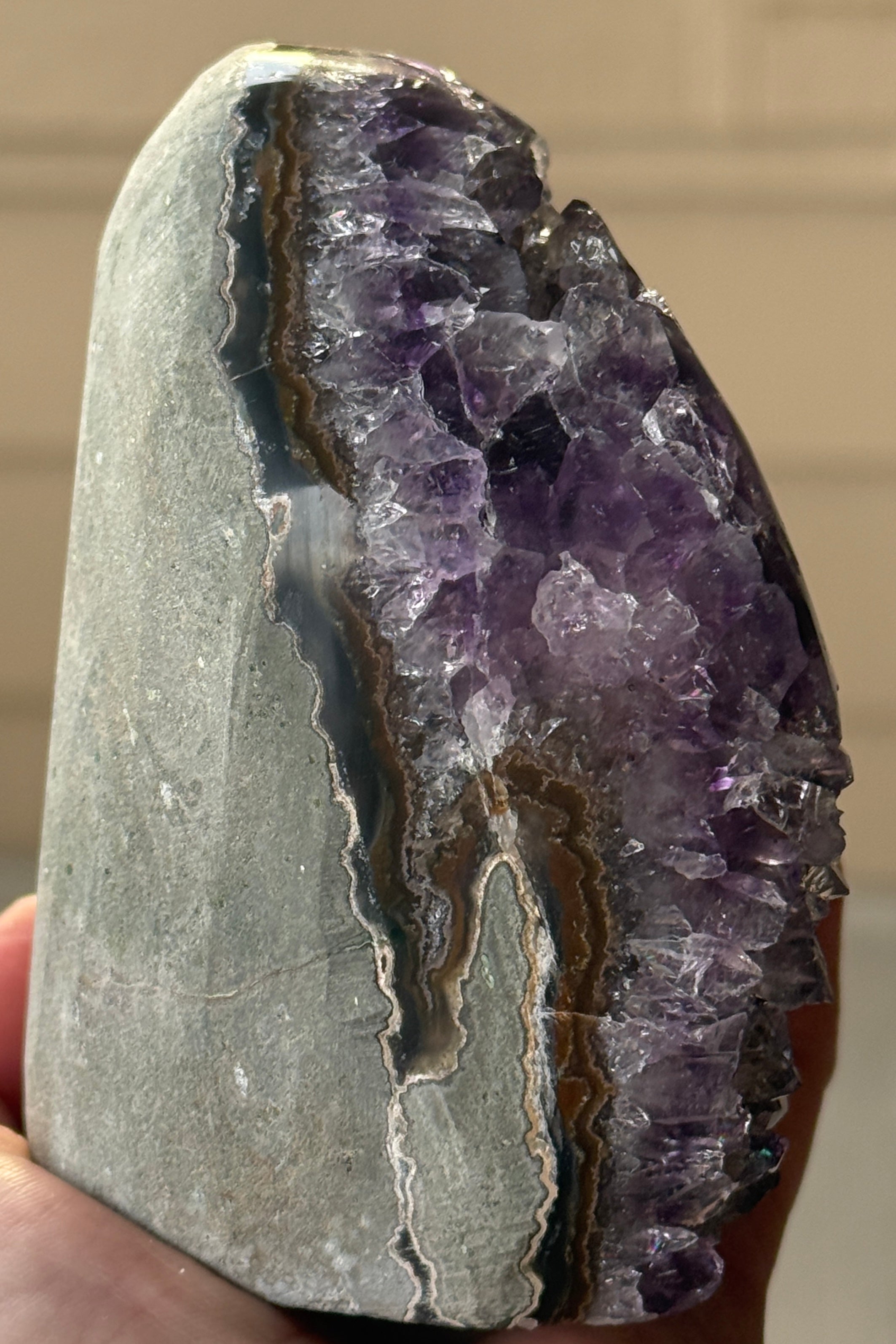 A polished amethyst geode with a deep purple hue. The crystal formation is visible, with numerous small, sparkling points. A dark, circular inclusion is present near the base, adding contrast to the overall color. The geode is a natural, decorative item.