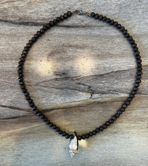 A beaded necklace made of small dark brown beads with a conch shell pendant, displayed on a weathered wood background.