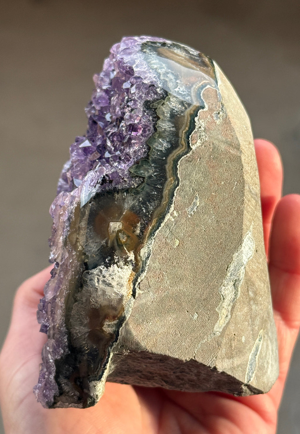 A polished amethyst geode with a deep purple hue. The crystal formation is visible, with numerous small, sparkling points. A dark, circular inclusion is present near the base, adding contrast to the overall color. The geode is a natural, decorative item.