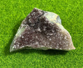 A natural amethyst geode crystal cluster with a dark purple interior and sparkling crystal formations. The geode is set against a vibrant green background, showcasing its natural beauty.