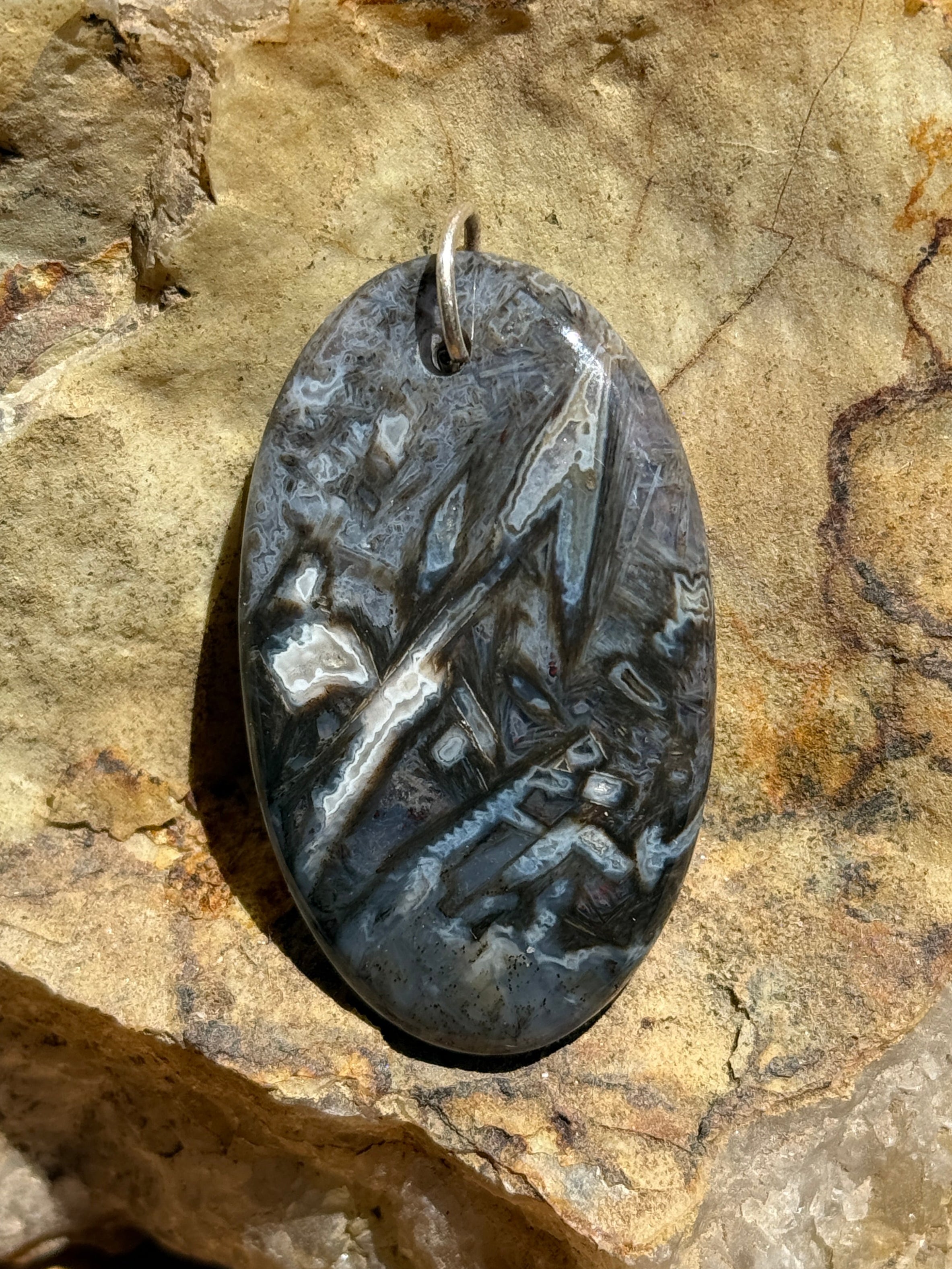 An oval pendant made of polished black and white agate with a silver bail, displayed on a textured natural stone against a wooden surface.