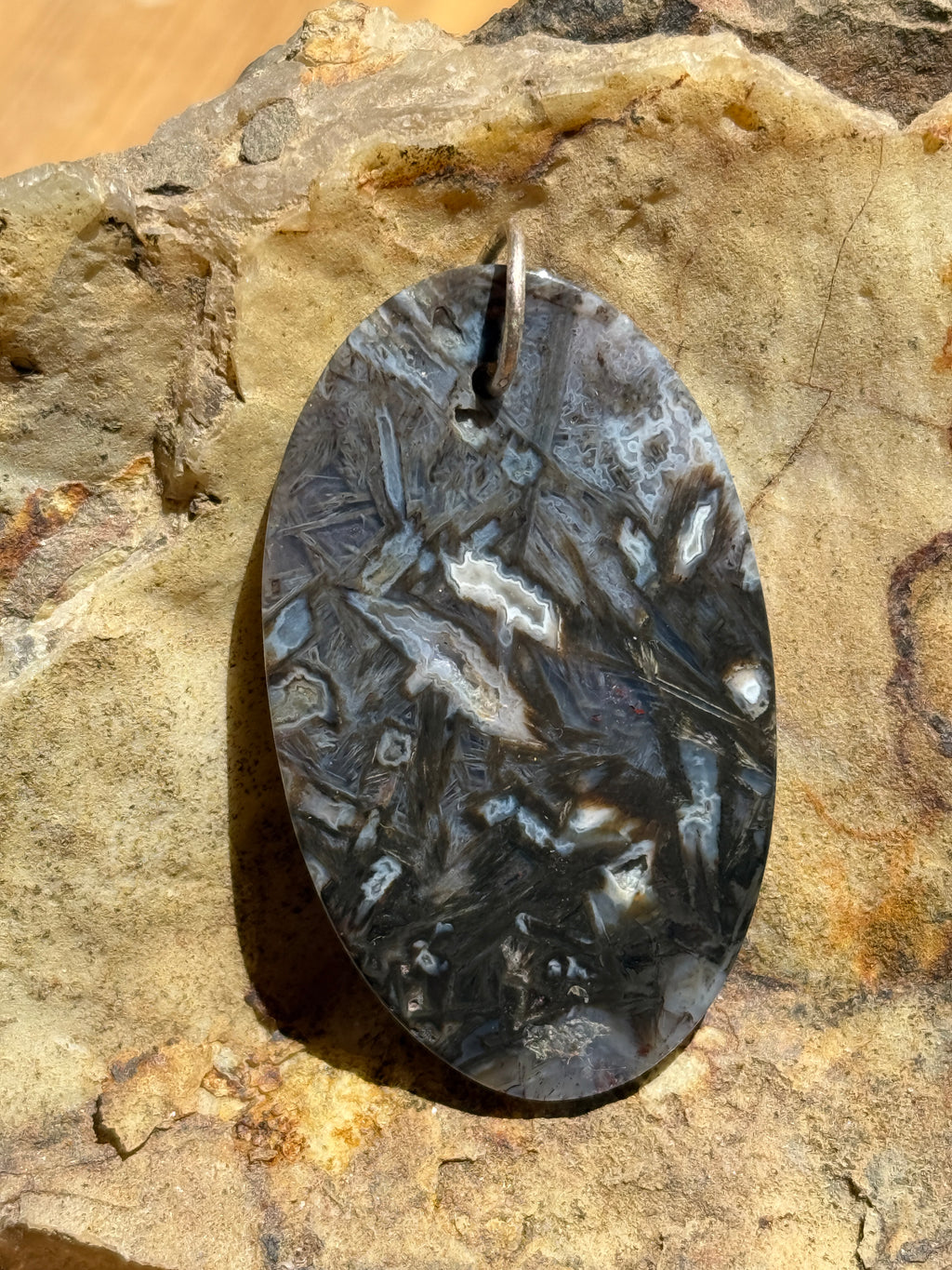 An oval-shaped pendant with a silver bail. The pendant features a marbled pattern of gray, white, and black