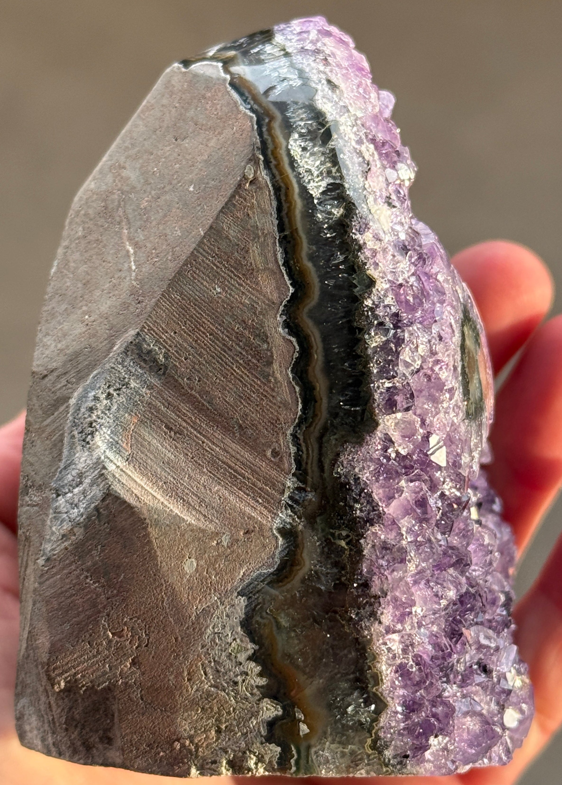 Close-up of a layered rock with purple crystal formation held by a hand.