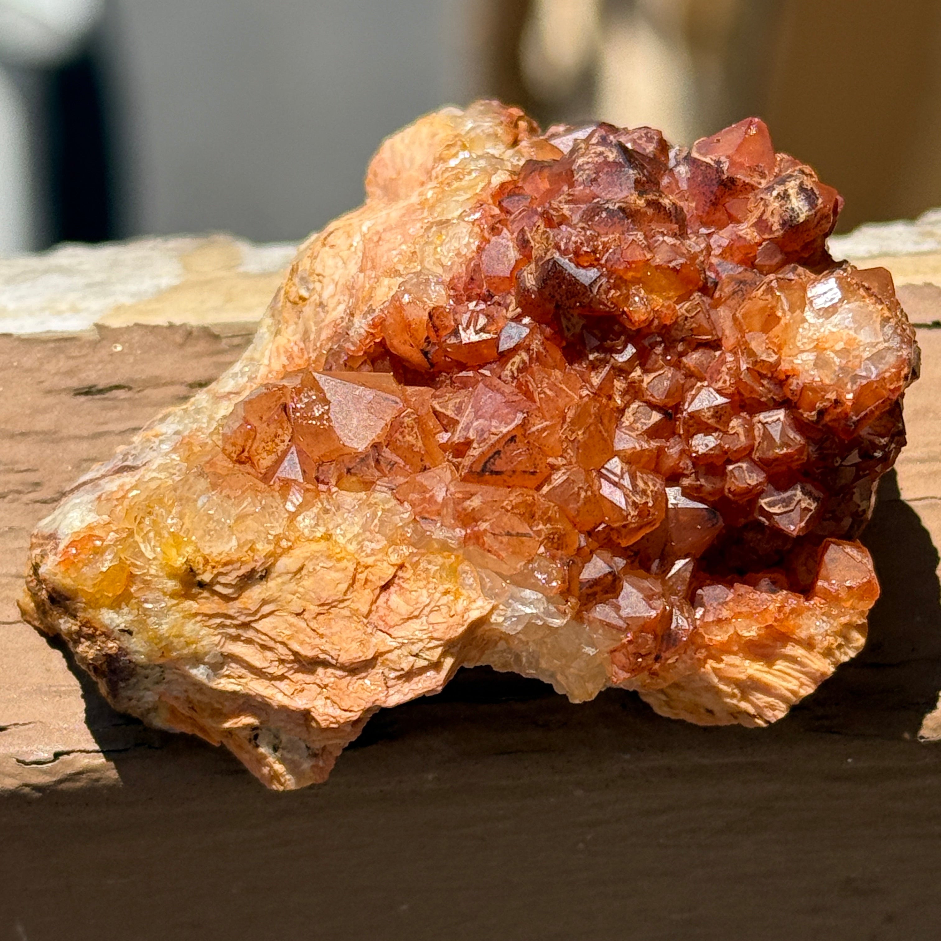 A natural crystal cluster with faceted orange-brown and amber translucent stones mounted on a weathered wooden post in outdoor sunlight.