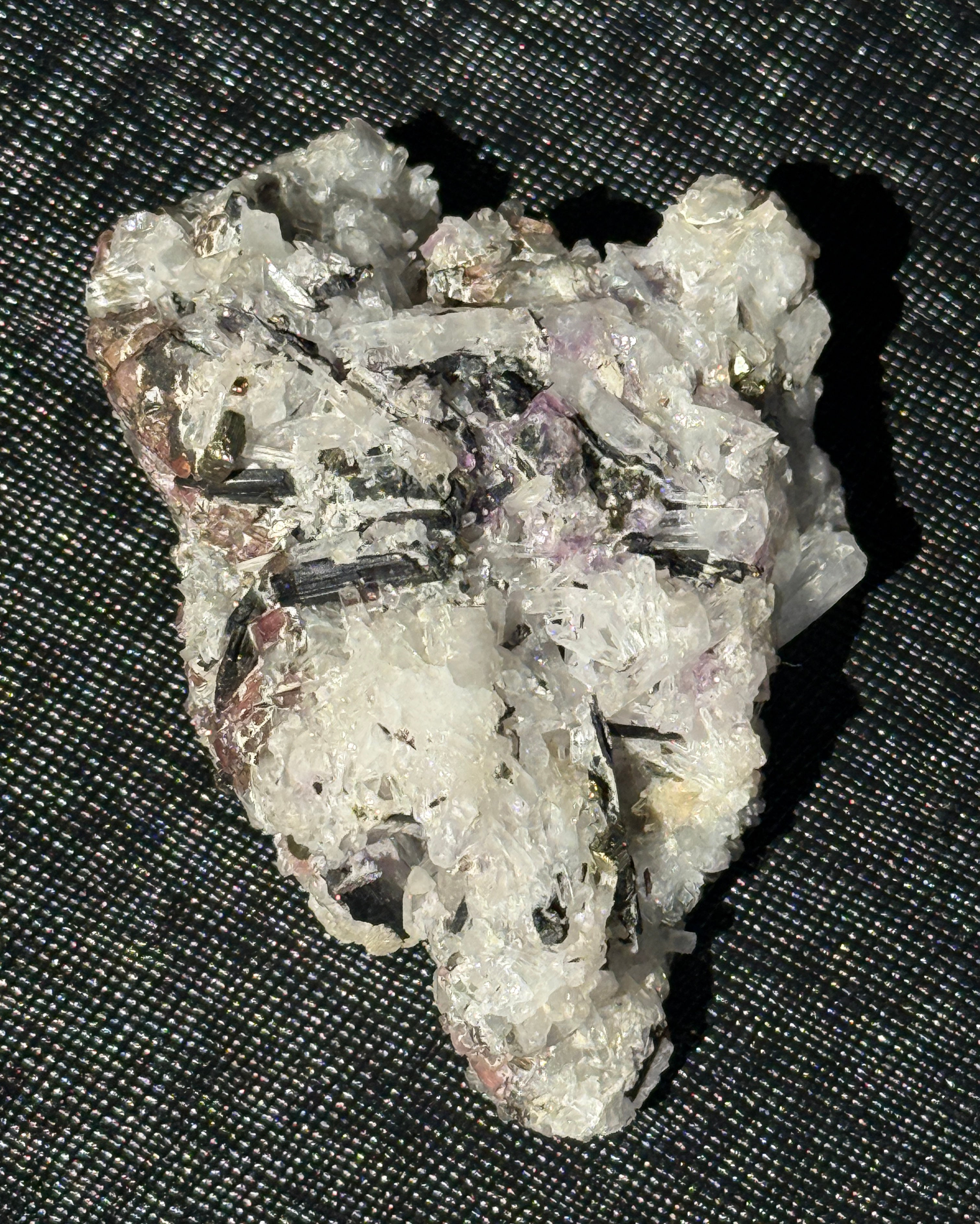 A raw mineral specimen featuring white quartz crystals and metallic gold flecks, resting on a black textured mesh background.