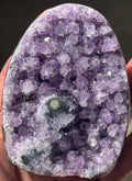 A polished amethyst geode, showcasing a rich purple hue with crystalline formations. The geode has a rounded top and a flat base, revealing the natural beauty of the gemstone.