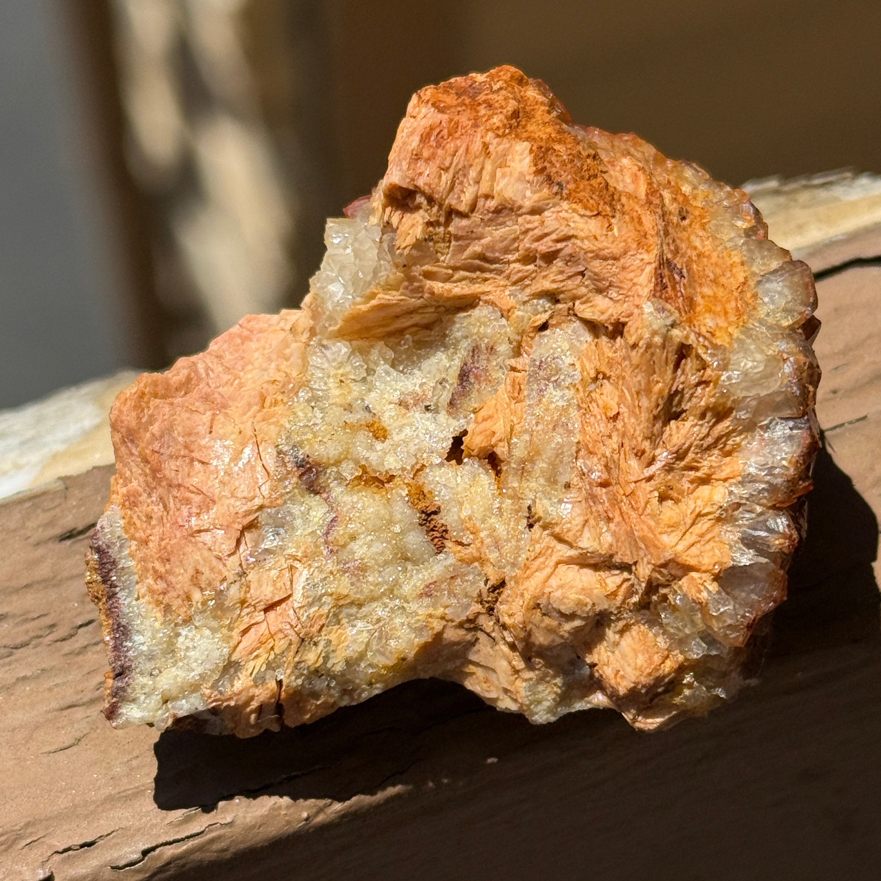 A close-up of a rough, textured mineral or rock specimen with orange, tan, and cream tones, attached to a wooden surface in natural light.