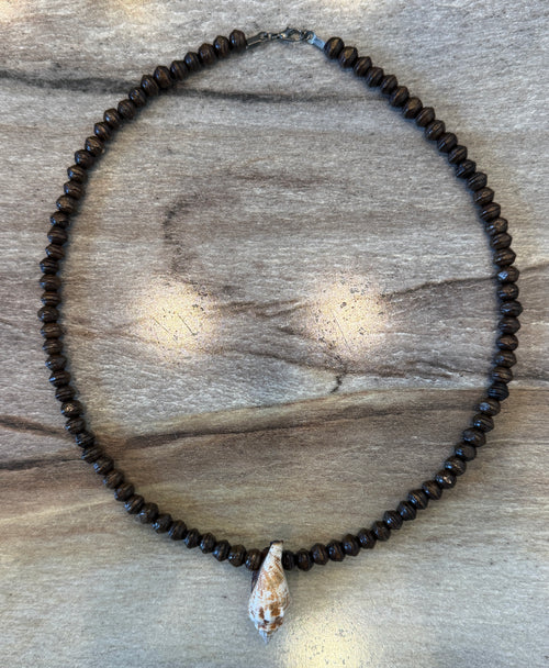 A beaded necklace made of small dark brown beads with a white seashell pendant, displayed on a gray wood background.