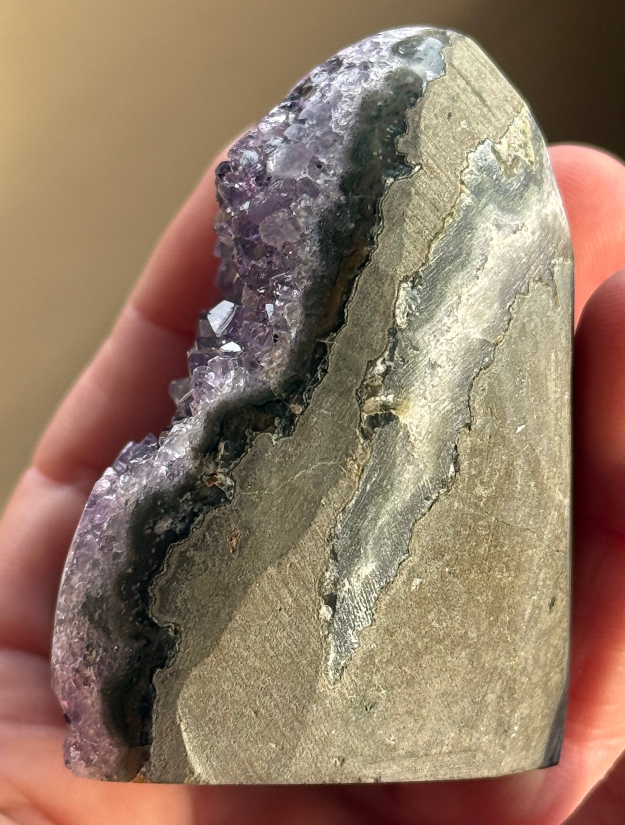 A polished amethyst geode with a deep purple hue. The crystal formation is visible, with numerous small, sparkling points. A dark, circular inclusion is present near the base, adding contrast to the overall color. The geode is a natural, decorative item.