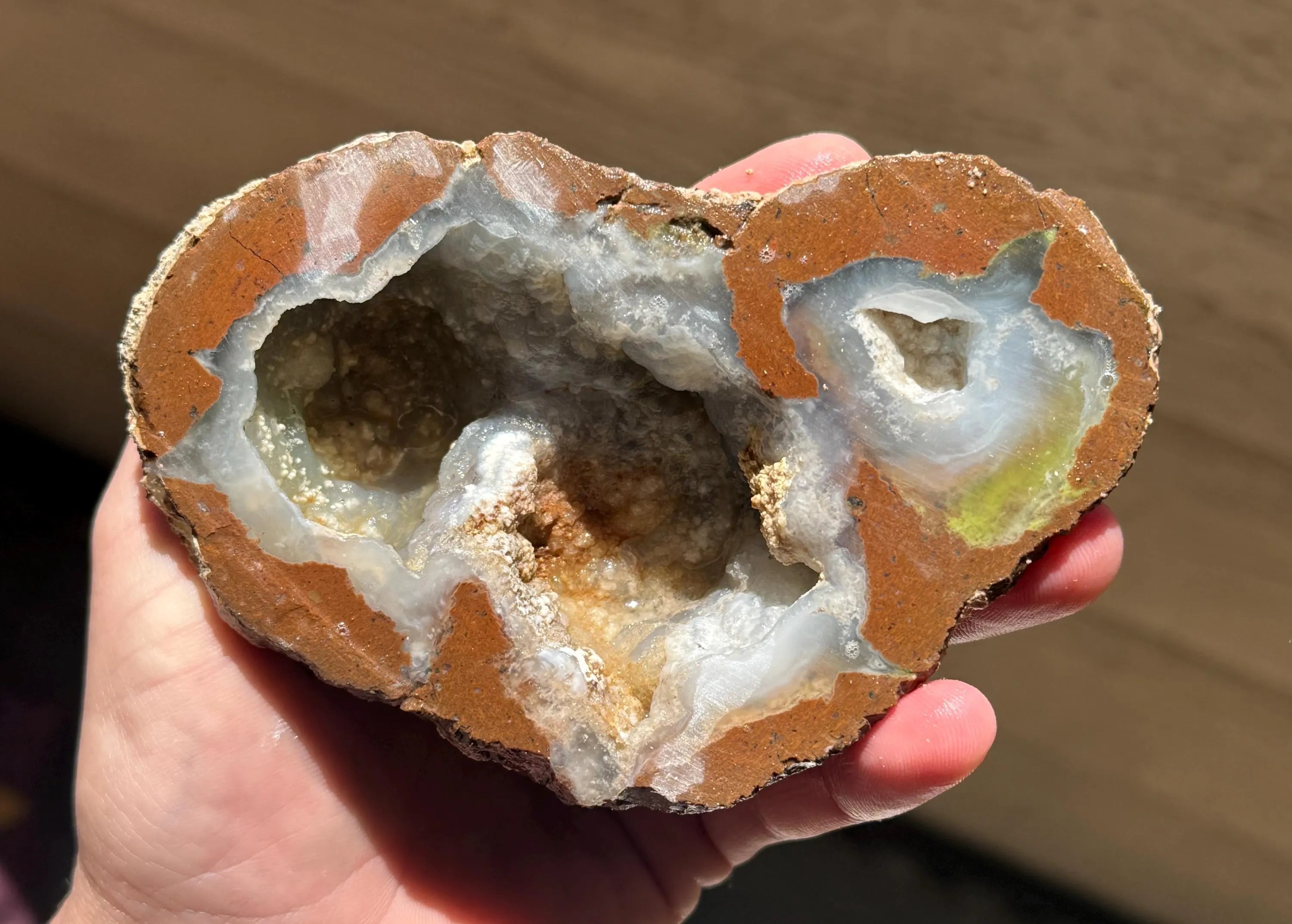 Thunder egg geode, showcasing a natural formation. The outer layer is a reddish-brown matrix, framing a cavity filled with crystalline structures and a light blue and green interior. 